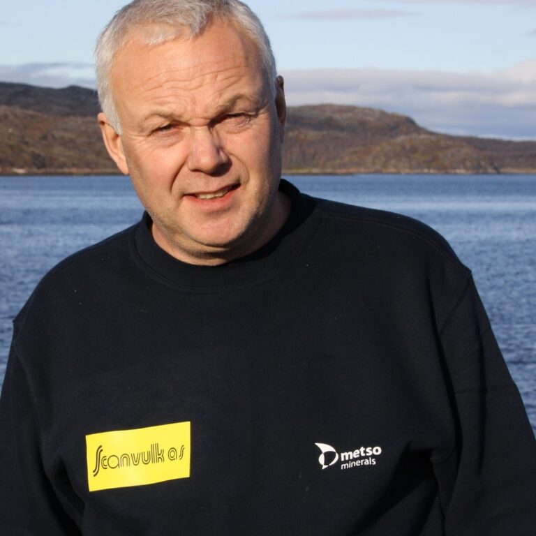 Terje Hansen, i sort genser. Smilende. I bakgrunnen hav og fjell. Foto.