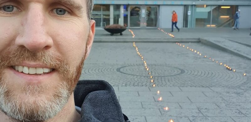 Mairus Nilsen, selfie foran bygg med fakler i forkant. Foto. Mairus Nilsen, selfie foran bygg med fakler i forkant. Foto.