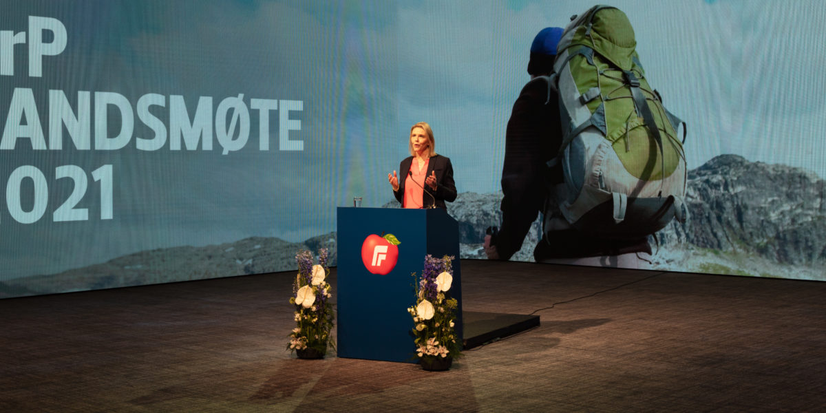 Sylvi Listhaug på talerstolen på FrPs landsmøte i 2021. Bak henne en LED-skjerm med bilde av en turgåer med grønn sekk.