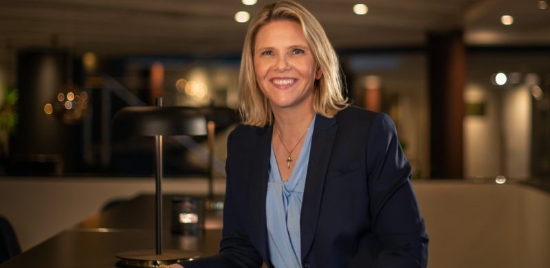 Sylvi Listhaug, smilende i blå dressjakke og lyseblå overdel. Lener seg svakt fremover mot et bord. Uskarp bakgrunn. Foto. Sylvi Listhaug, smilende i blå dressjakke og lyseblå overdel. Lener seg svakt fremover mot et bord. Uskarp bakgrunn. Foto.