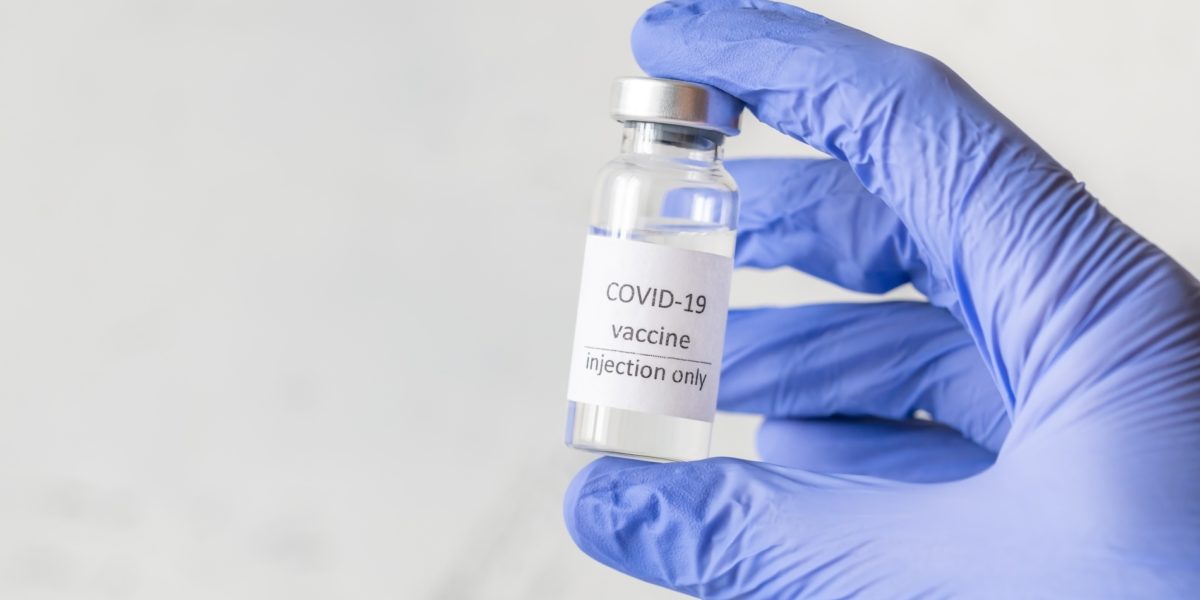 Hånd med blå engangshanske som holder en ampull med teksten Covid-19 vaccine injection only. Foto