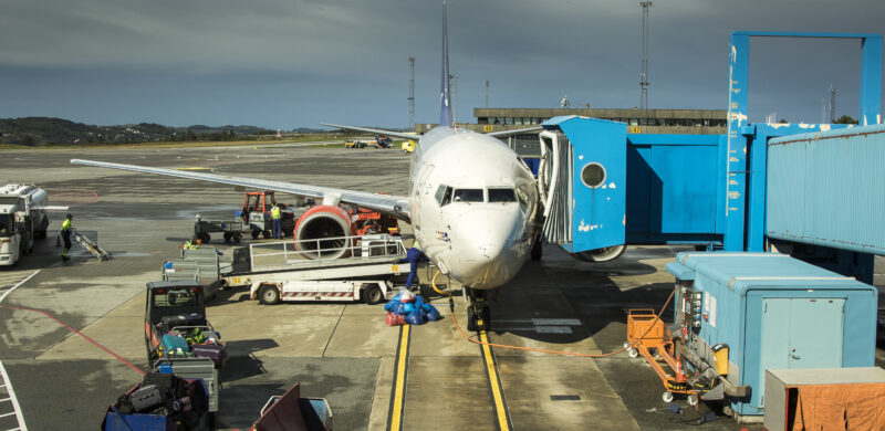 Fly som er dokket til på en flyplass. Flere kjøretøy står rundt. Foto. Fly som er dokket til på en flyplass. Flere kjøretøy står rundt. Foto.