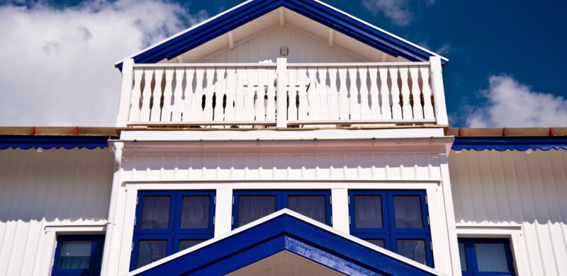 Stort hvitt hus med blå lister og møner, sett nedenfra mot blå himmel. Foto. Stort hvitt hus med blå lister og møner, sett nedenfra mot blå himmel. Foto.