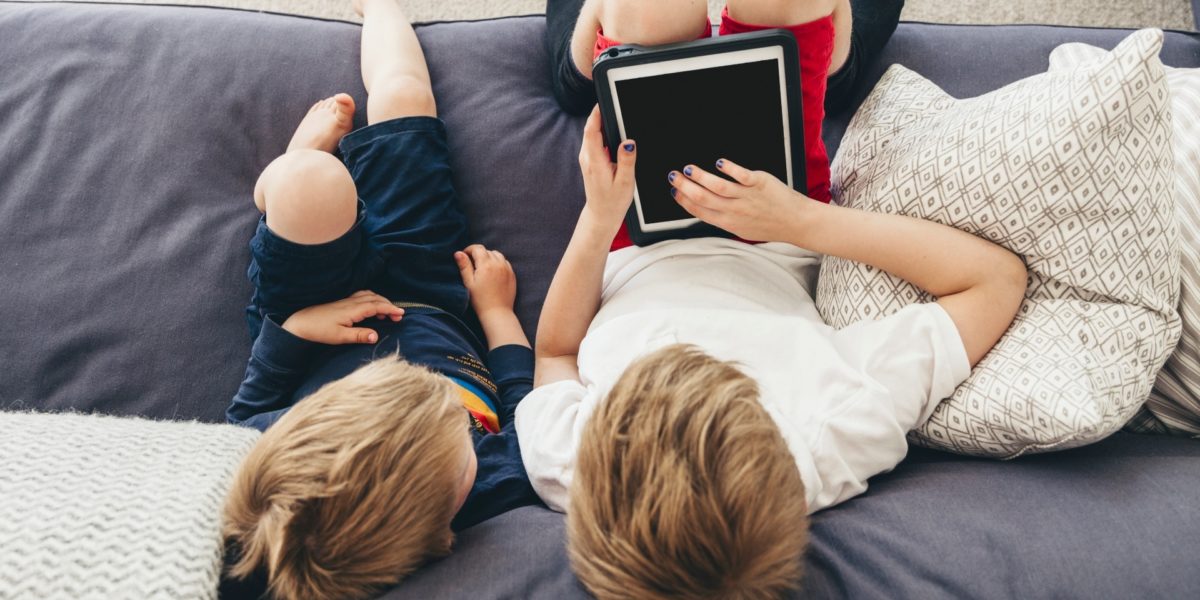 To barn sitter i en sofa. Den ene har holder en ipad i hendene som begge ser på. Foto. To barn sitter i en sofa. Den ene har holder en ipad i hendene som begge ser på. Foto.