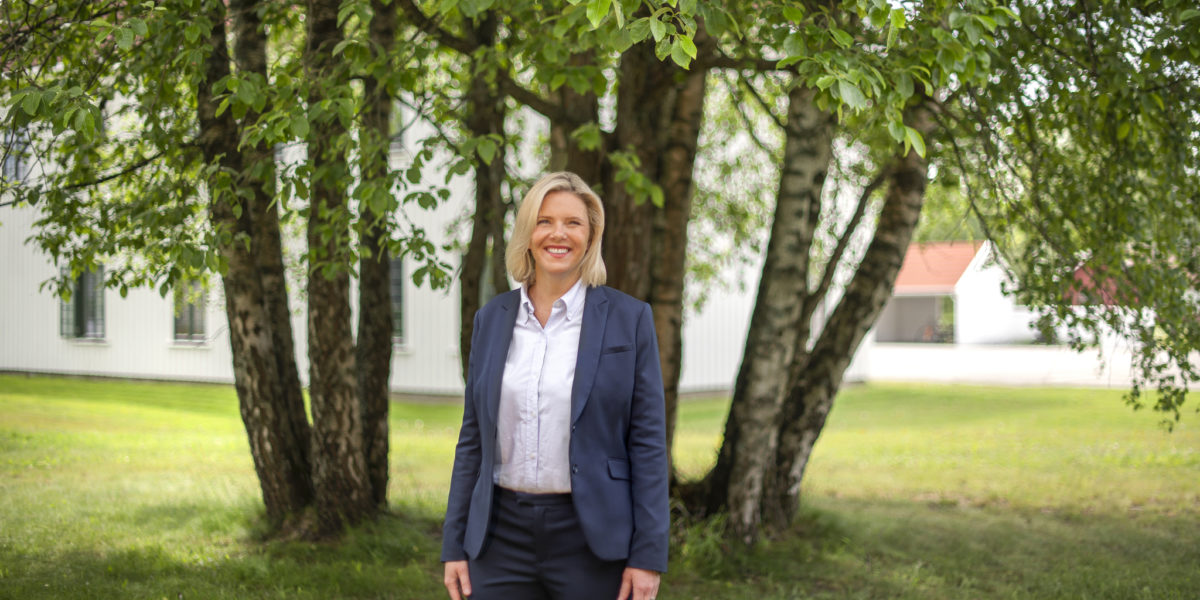 Sylvi Listhaug, smilende ikledd dressjakke. I bakgrunnen grønne trær. Foto. Sylvi Listhaug, smilende ikledd dressjakke. I bakgrunnen grønne trær. Foto.